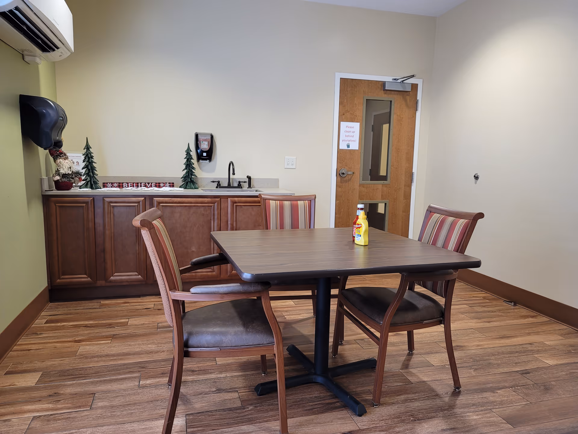 Dining area in a senior living facility with a table, four chairs, and a kitchenette counter.