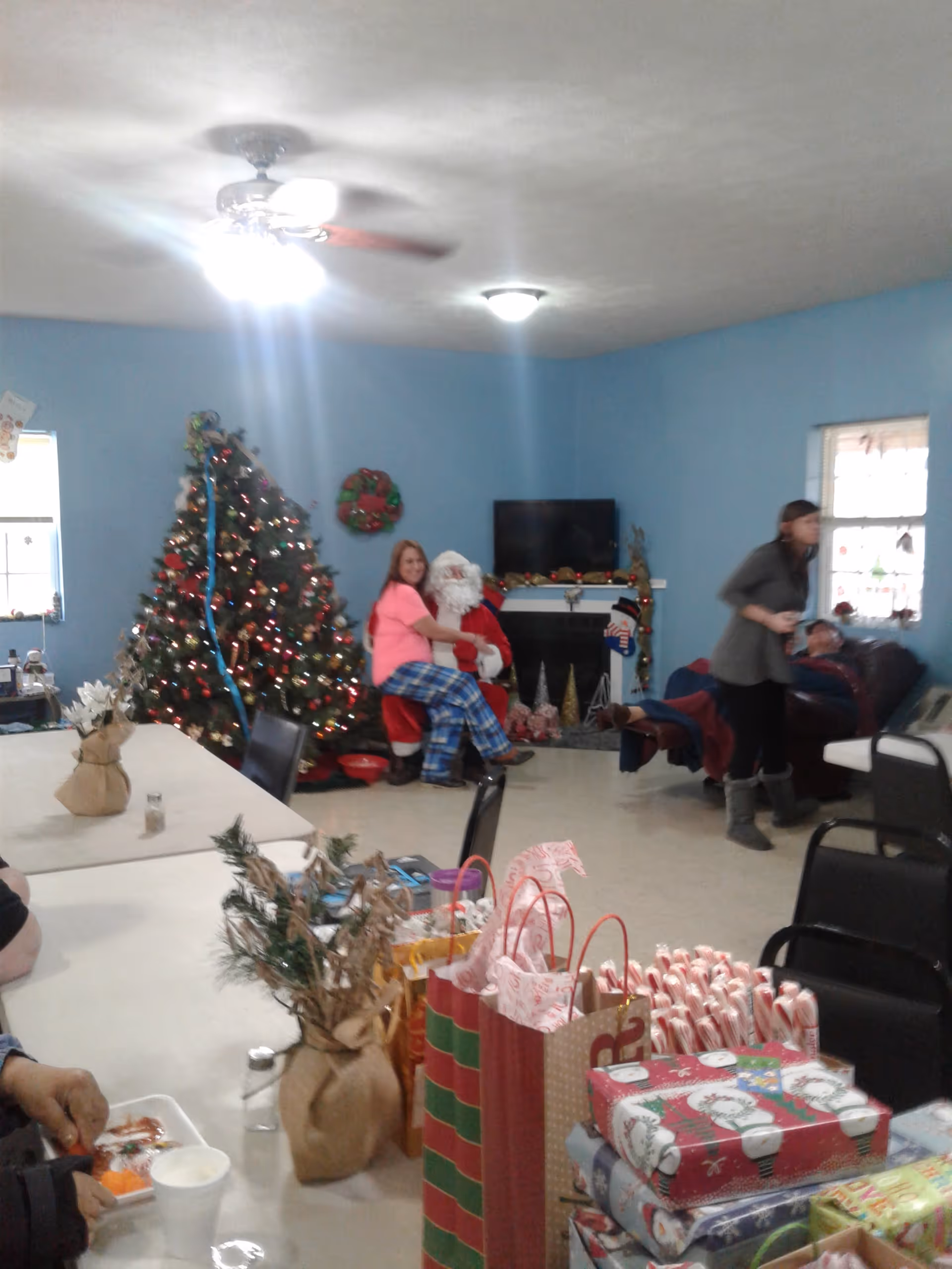 A decorated senior living room with a Christmas tree, gifts, and people around Santa.