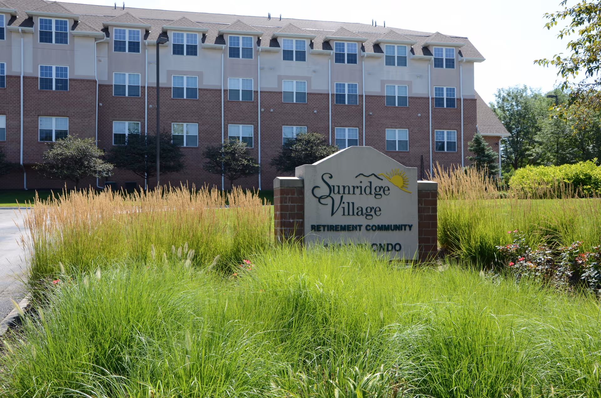 Sunridge Village retirement community building exterior with a stone entrance sign and landscaped grounds