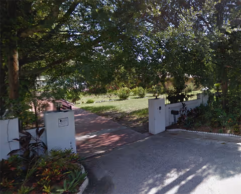 Entrance to a residential outdoor area with a gate, path, and shaded garden.