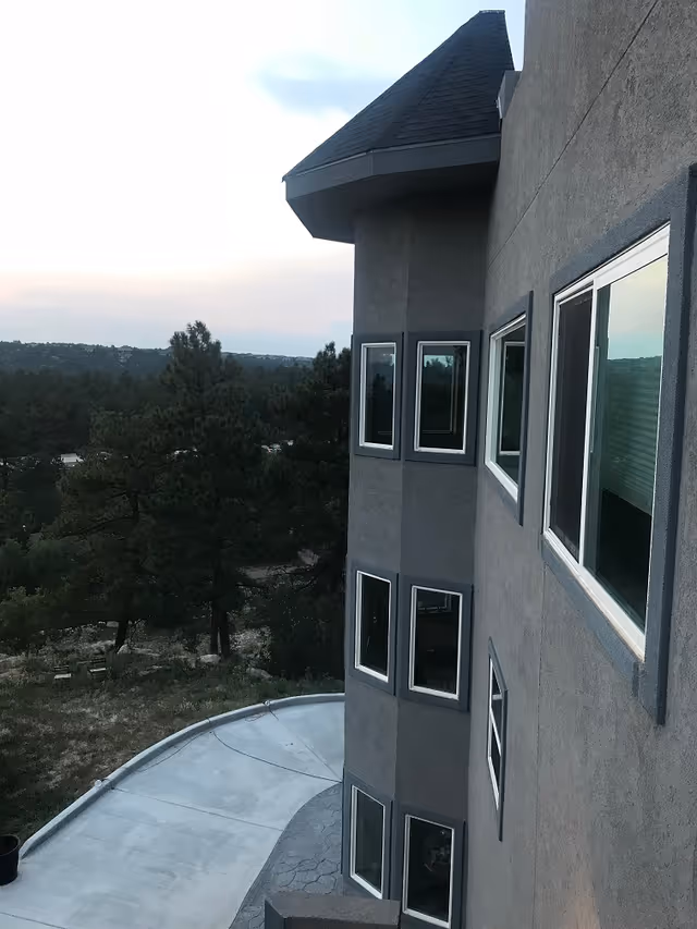 Gray multi-story building exterior with many windows overlooking a wooded landscape.