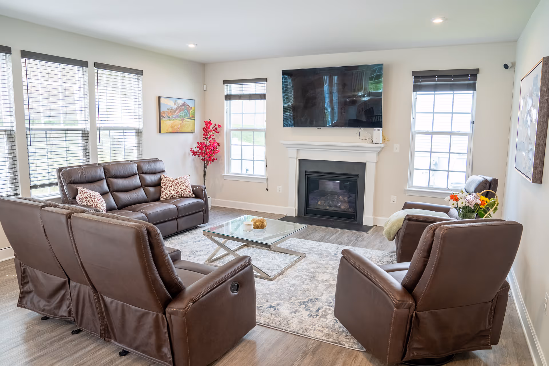 Bright living room with brown leather seating, glass coffee table, fireplace, and wall-mounted TV.