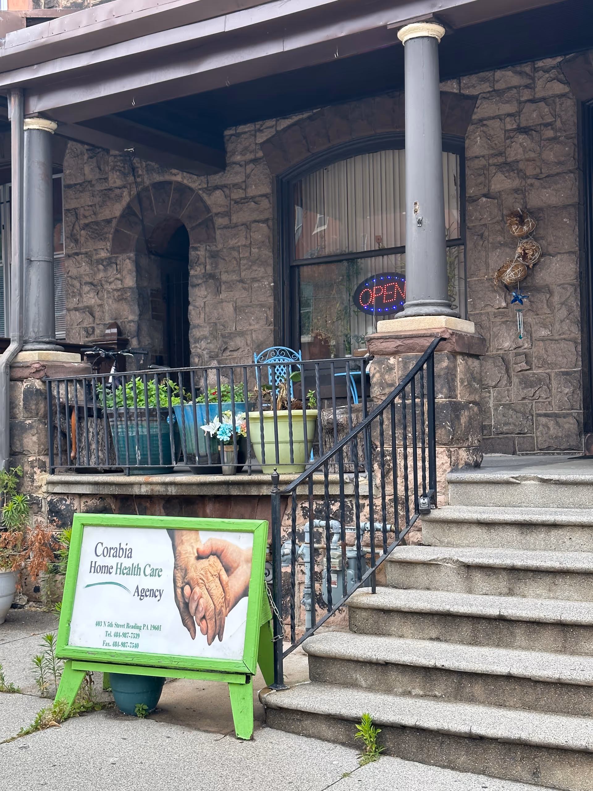 Stone storefront entrance with stairs, railing, potted plants, and a green sign outside Corabia.