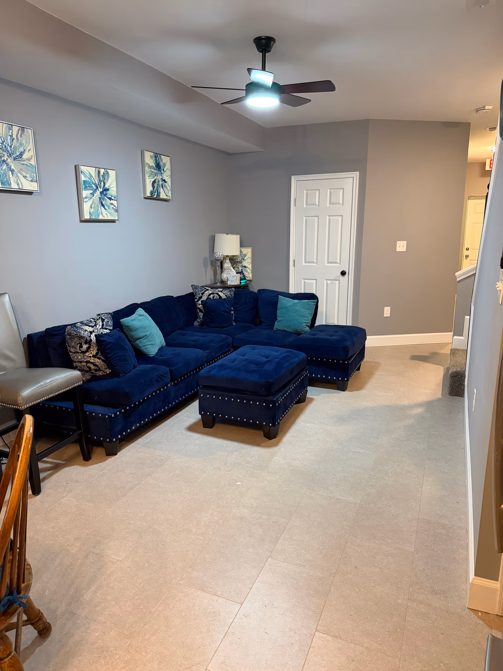 Blue velvet sectional and ottoman in a gray-walled senior living lounge.