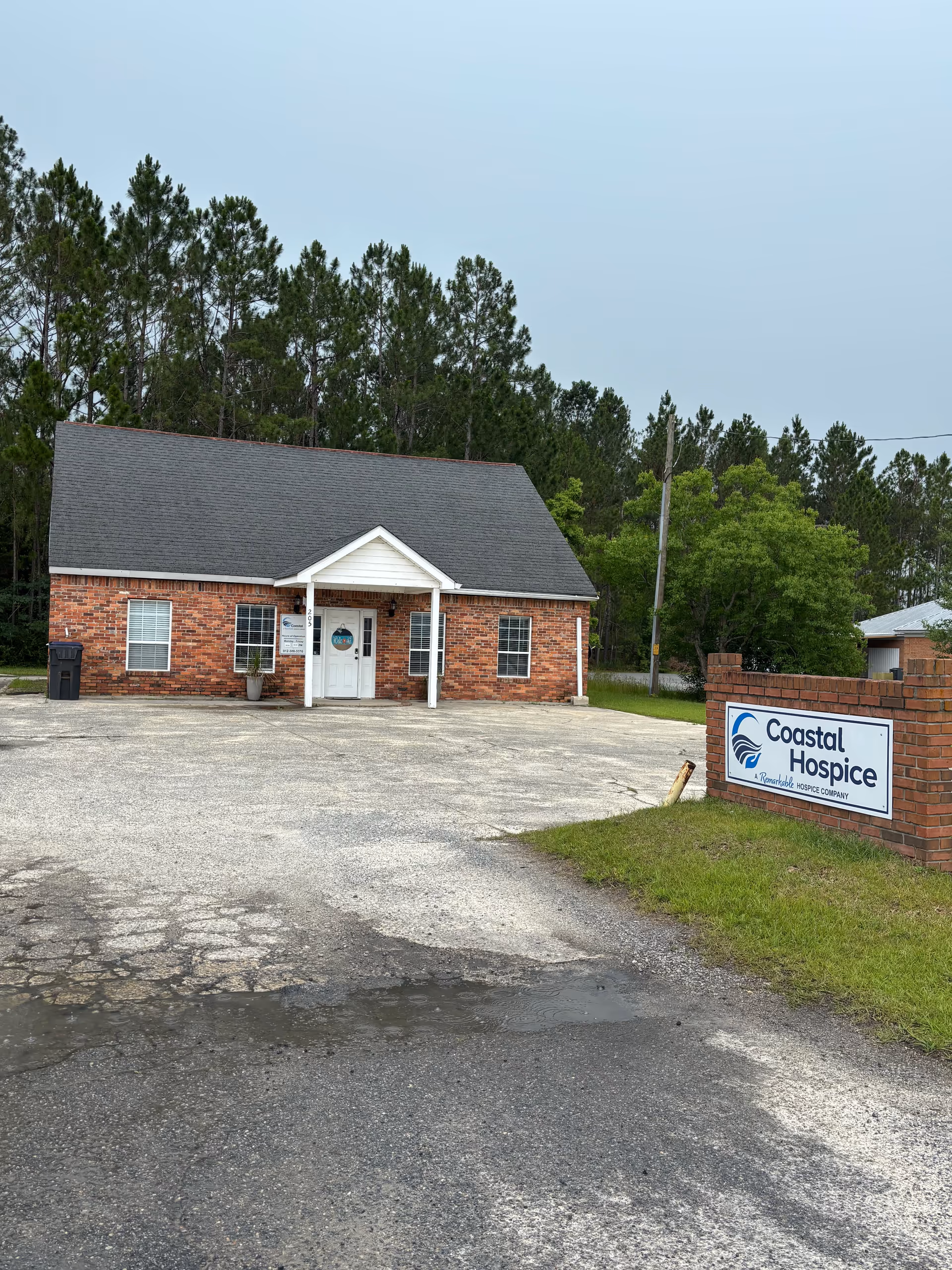Brick hospice building with a peaked roof and Coastal Hospice sign near the parking lot.