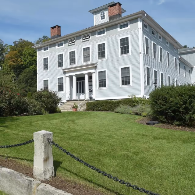 White multi-story senior living building with front entrance, columns, and manicured lawn.