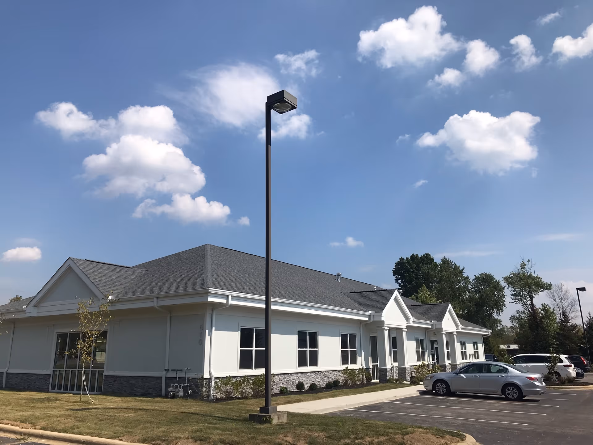 Single-story white senior living facility with a parking lot and tall streetlight under a blue sky.