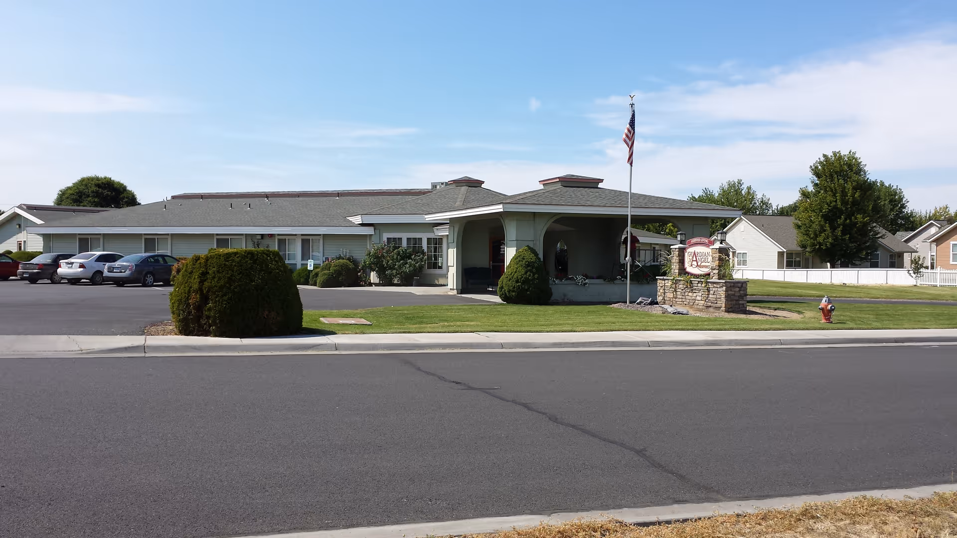 Single-story senior living facility front view with parking and American flag.