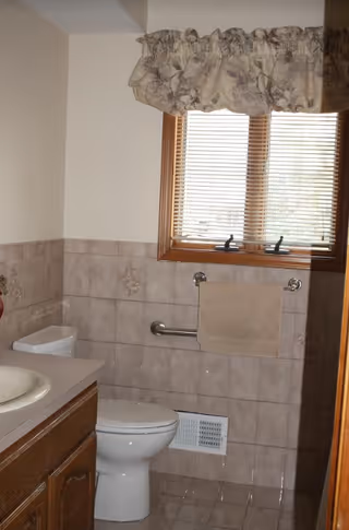 Small bathroom with toilet, sink, tiled walls, window with blinds, and towel bar.