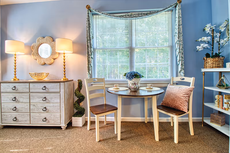 Bright, cozy dining nook with round table, two chairs, window, and decorative shelving.