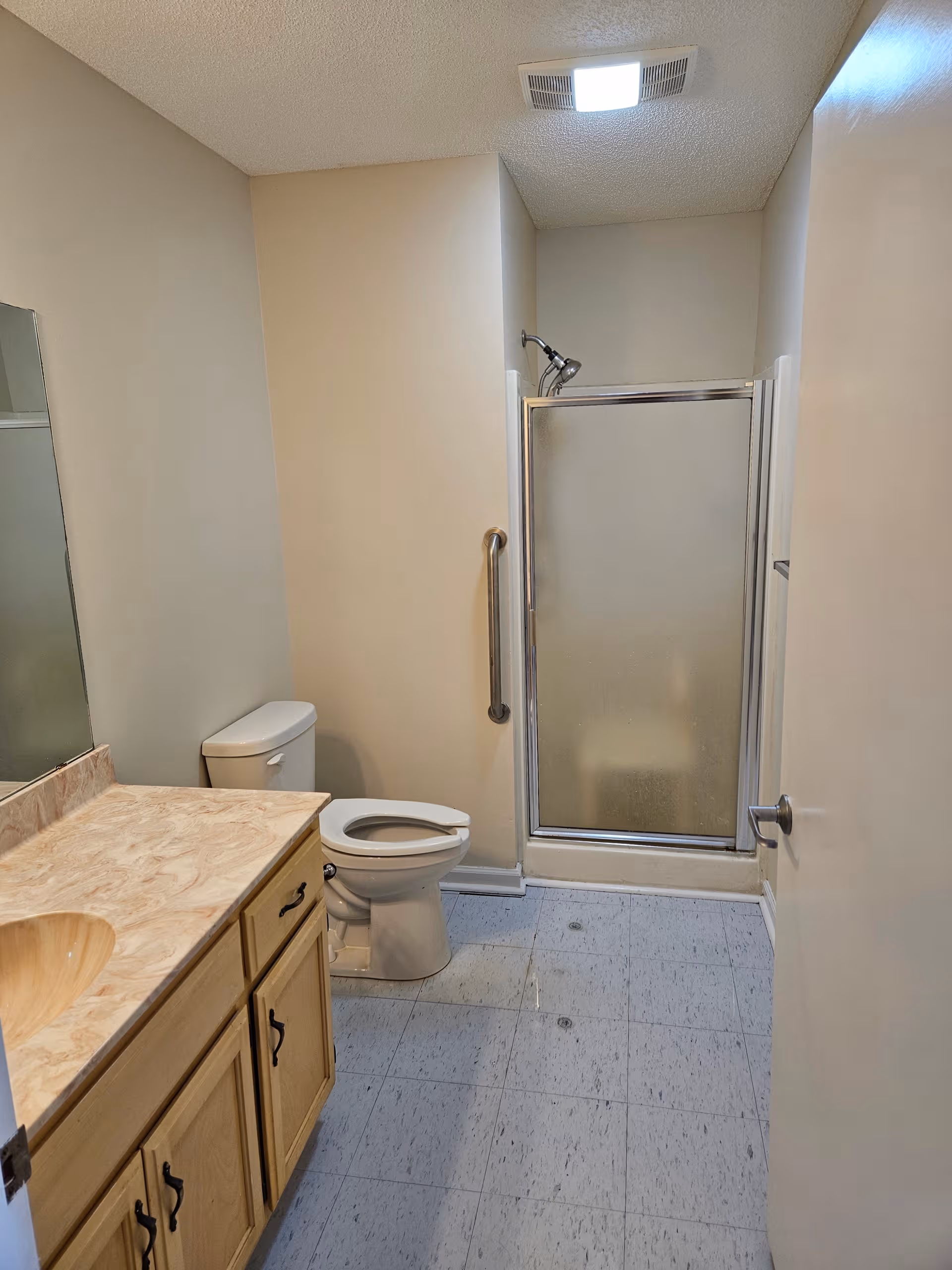 Compact bathroom with vanity, toilet, and glass-door shower in a senior living facility.