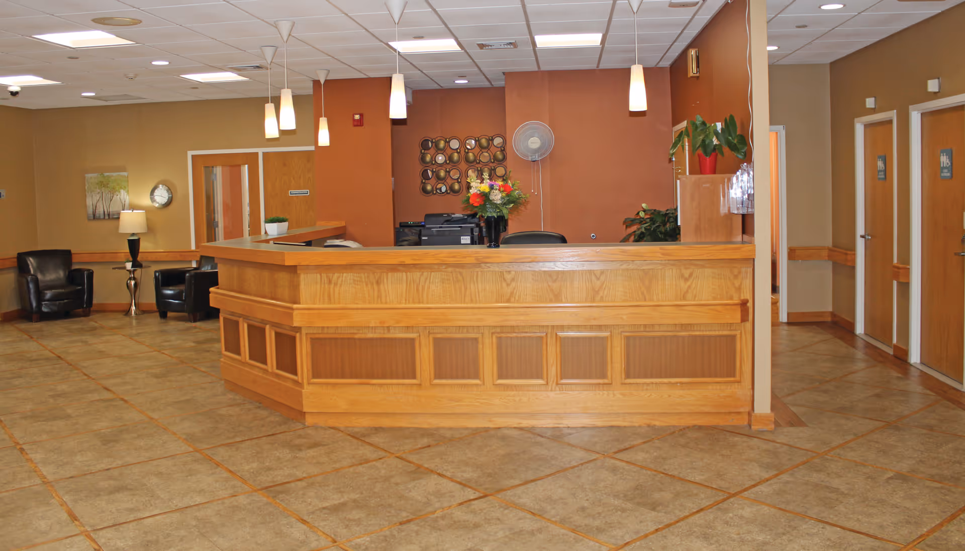 Wood reception desk in a facility lobby with pendant lights, tile floor and seating area.