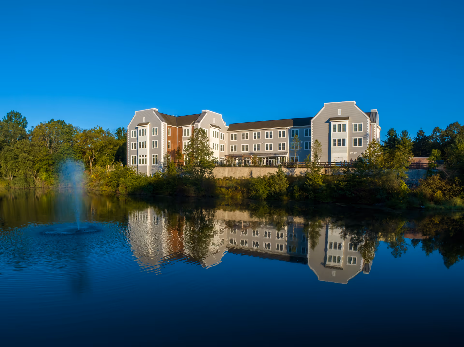 Exterior view of The Residence at Basking Ridge beside a lake with a fountain.