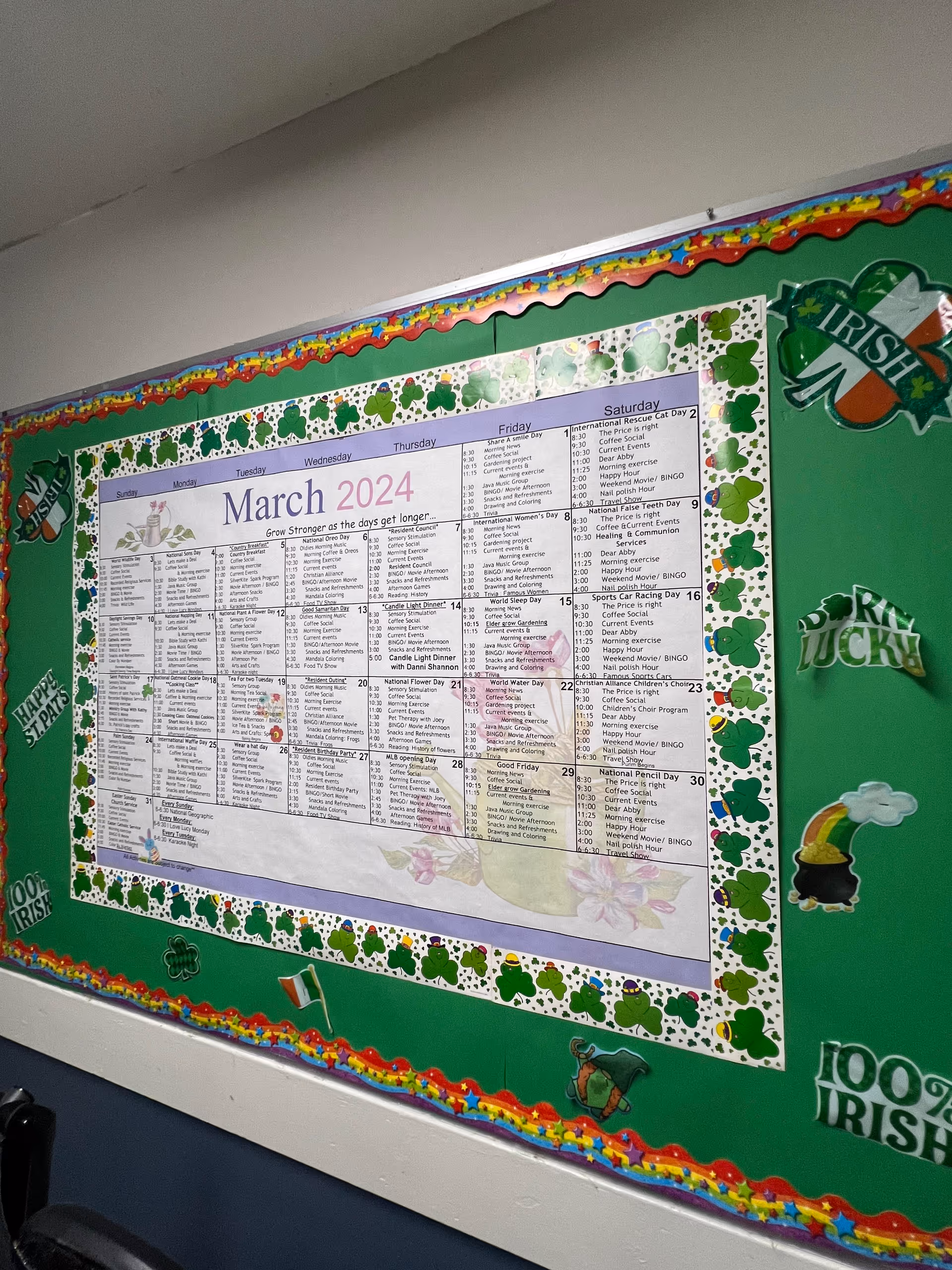 Indoor hallway wall with a large March 2024 calendar on a shamrock-bordered bulletin board.