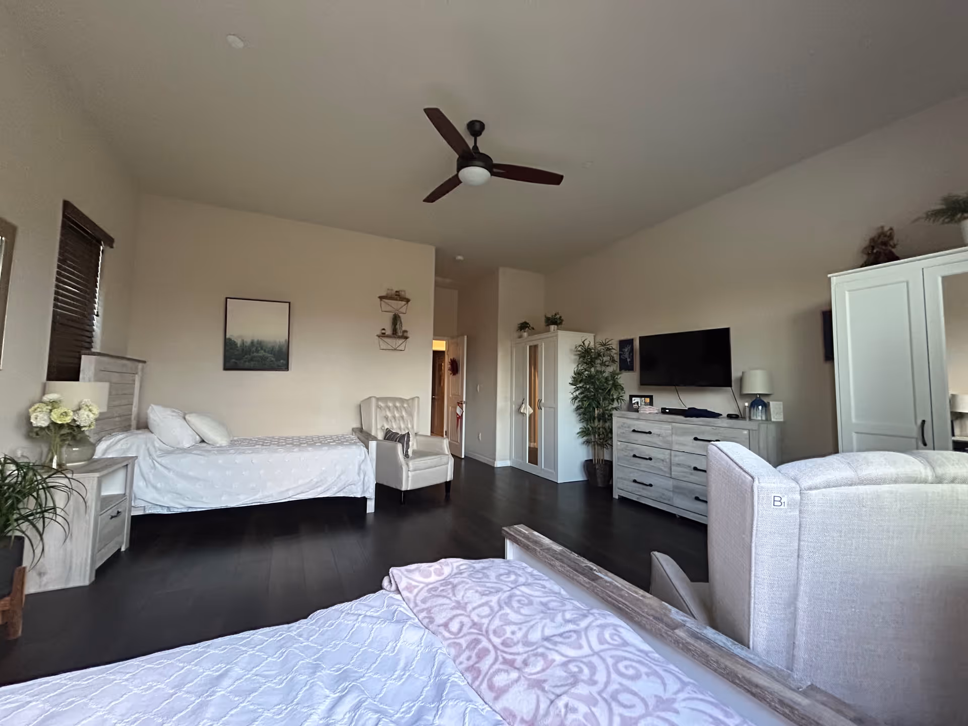 Spacious senior living suite with two beds, a dresser, TV, and seating.