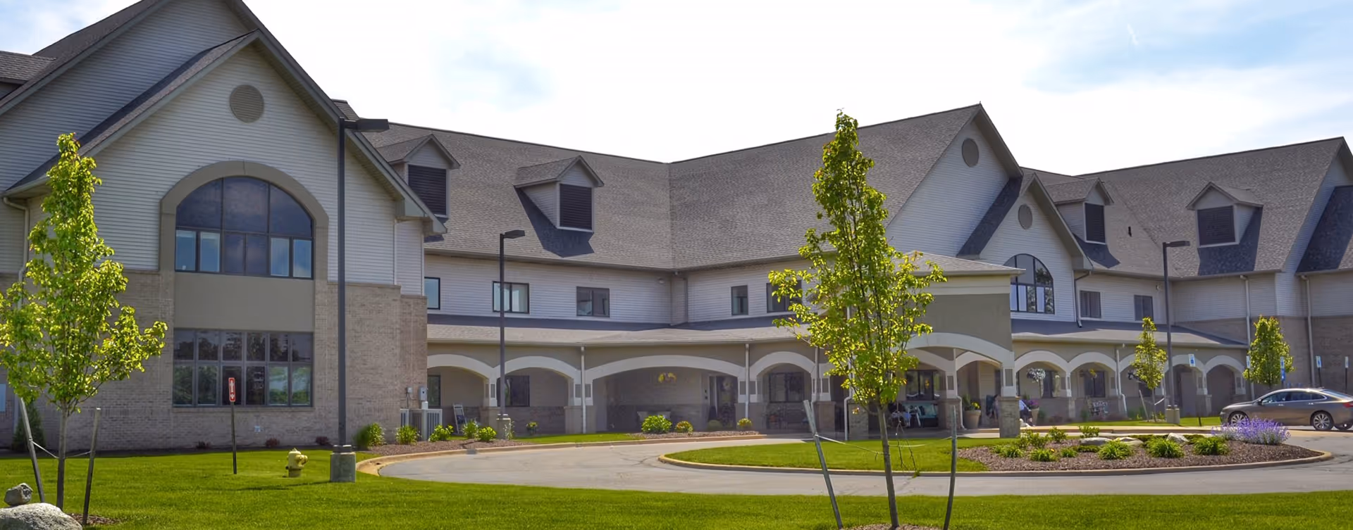 Exterior view of a senior living facility with arched entryway and landscaped front lawn.