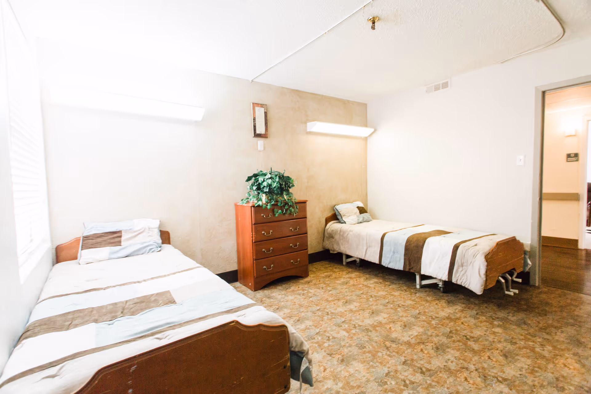 Two twin beds with a dresser between them in a small, well-lit bedroom.