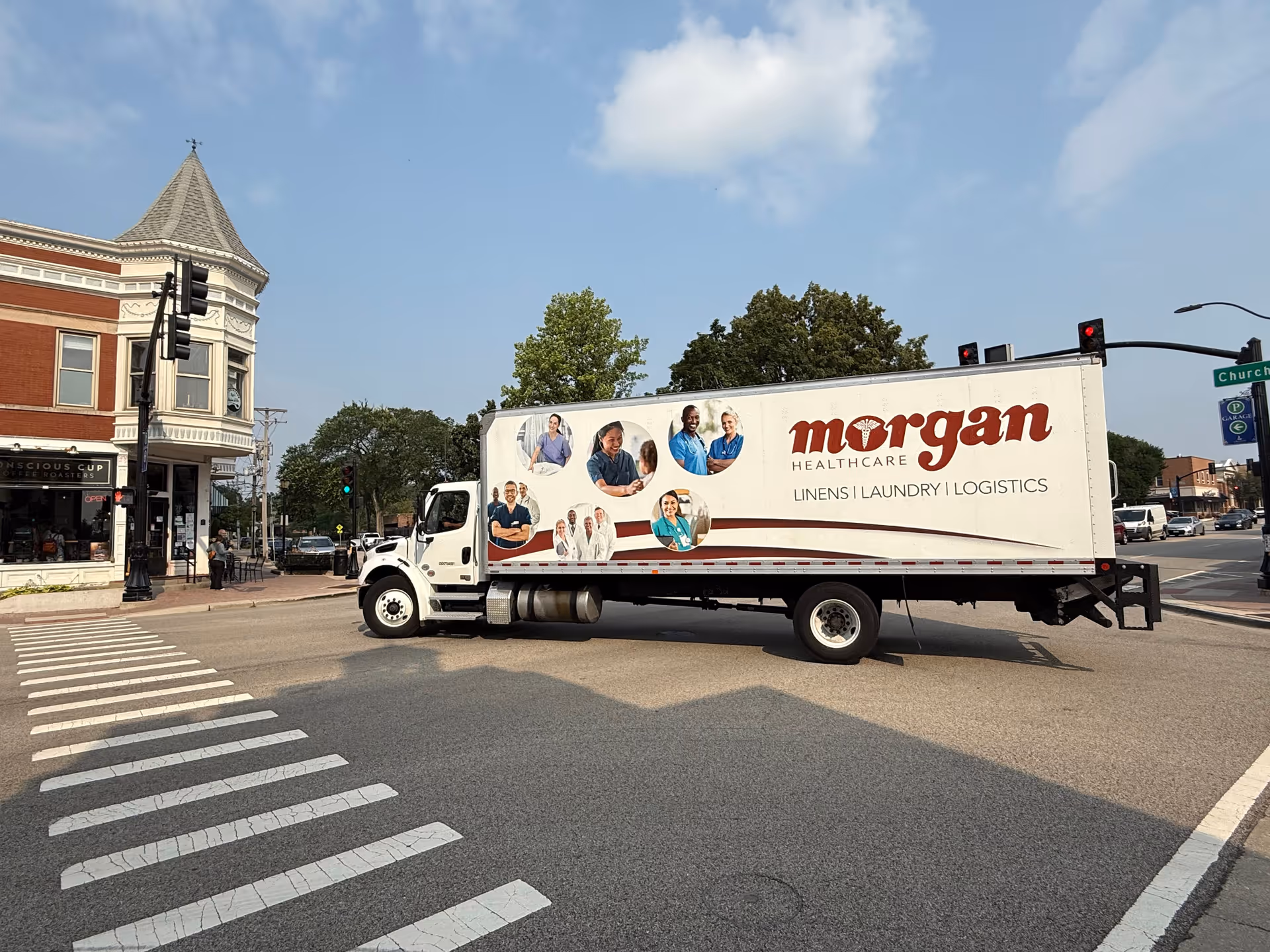 A white Morgan Healthcare delivery truck blocks a crosswalk on a small-town street.