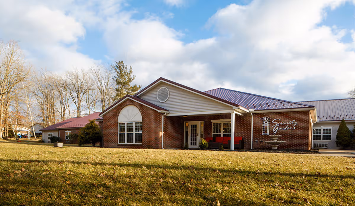 Brick senior living facility with a covered entry and Serenity Gardens sign.