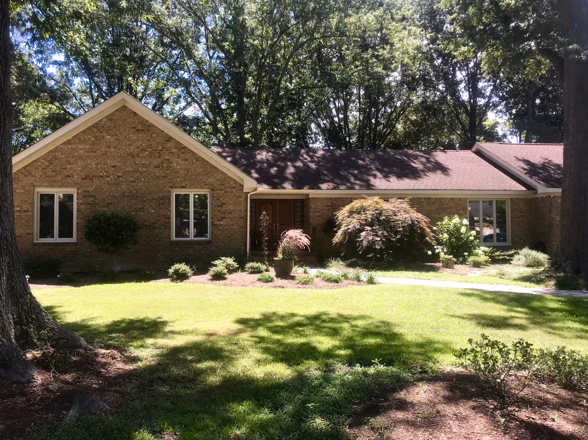 A single-story brick senior living facility with manicured lawn and trees in front.