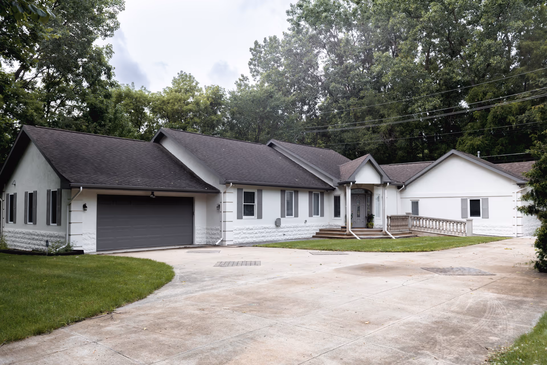 A white, single-story senior living facility with a long driveway and manicured lawn.