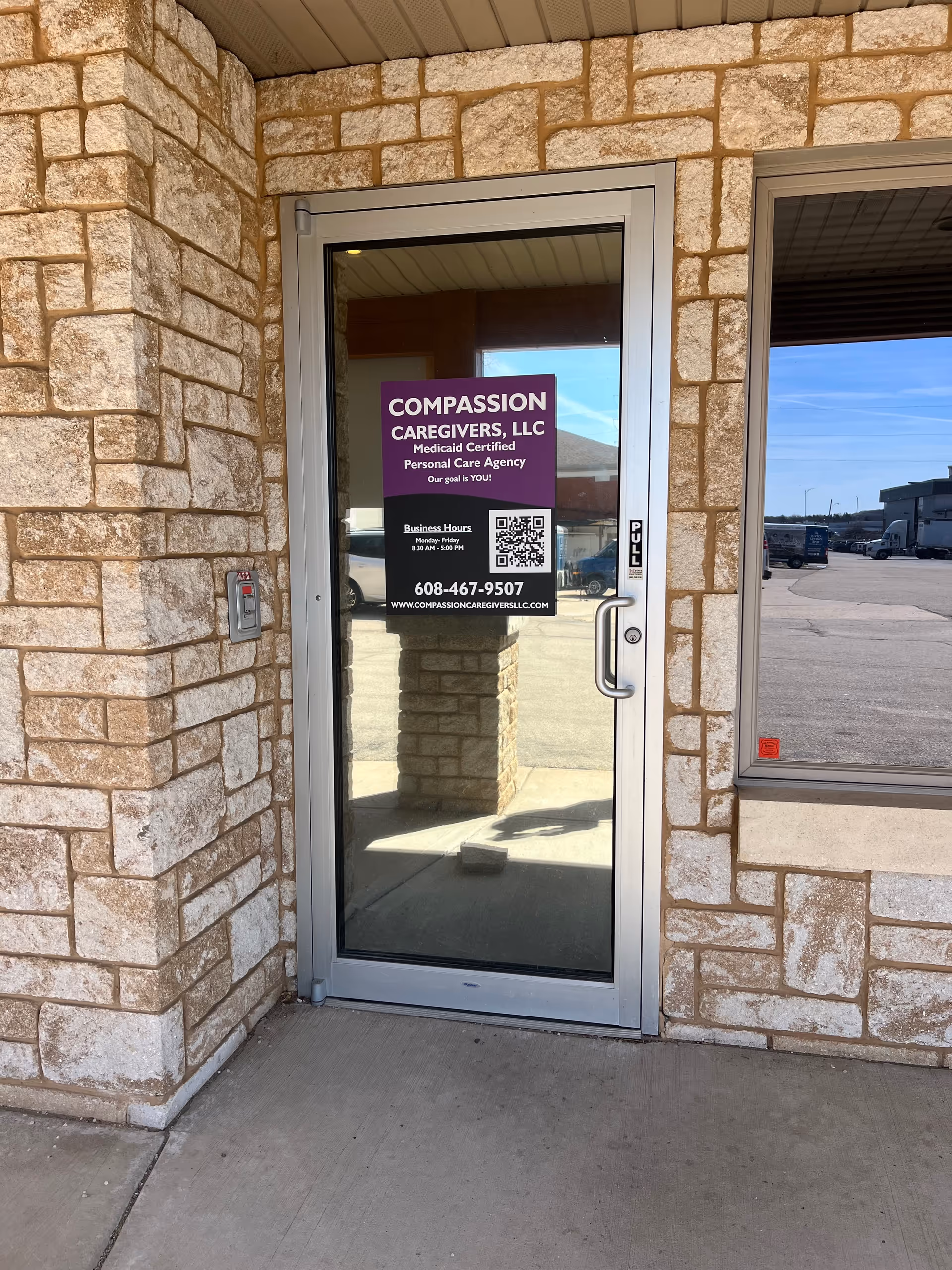 Glass door with a purple Compassion Caregivers LLC sign on a stone exterior.