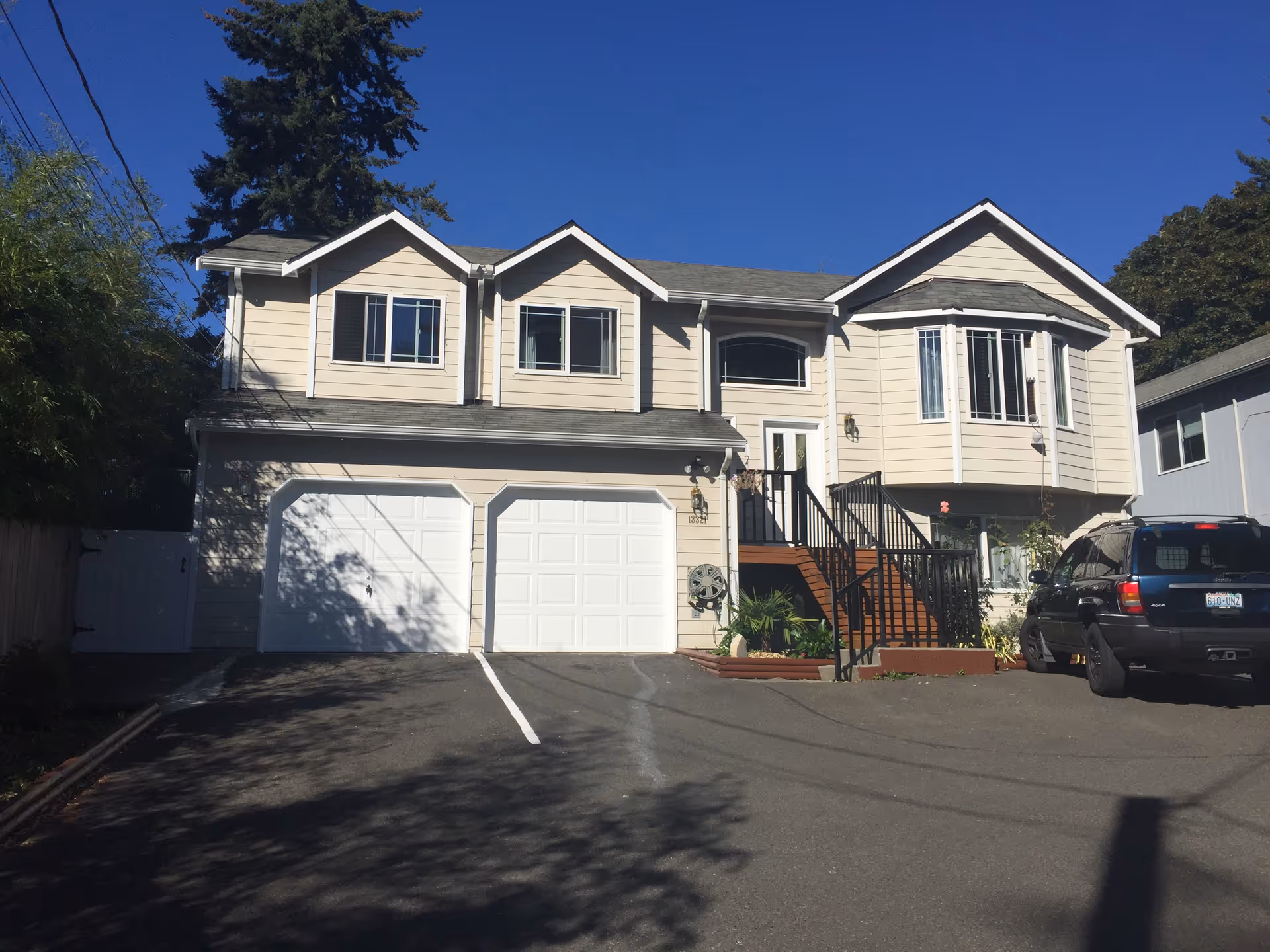 Two-story beige home with double garage doors, front stairs, and a parked SUV.