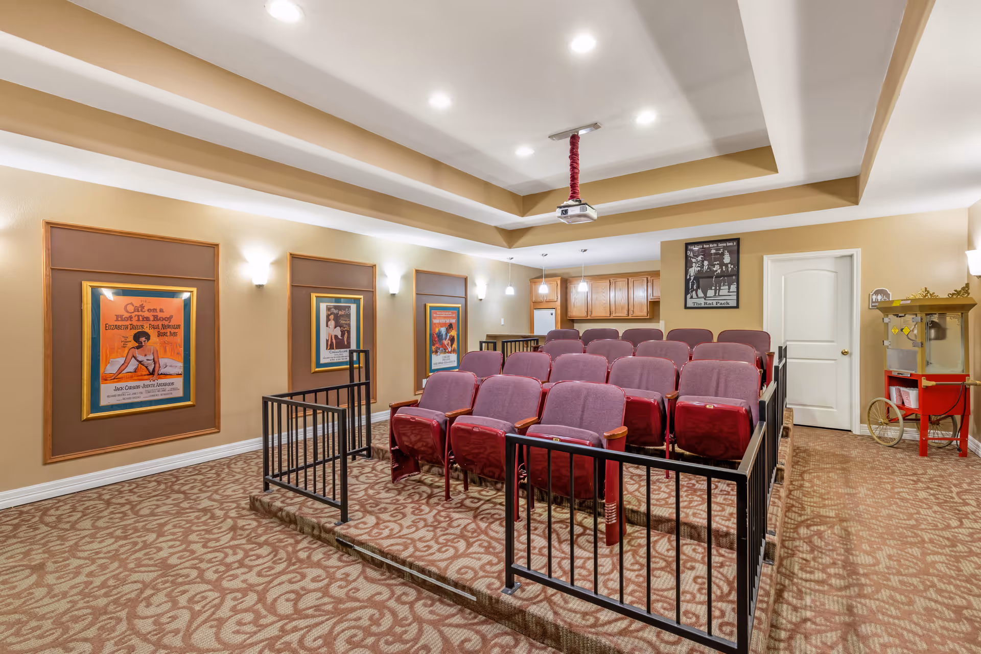Sunlit senior living theater with red cushioned seats, projector, posters, and a serving cart.
