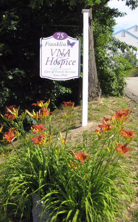 Outdoor sign for Franklin VNA Hospice amid blooming lilies and greenery.