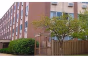 Multi-story brick senior living building with a fenced outdoor area and trees.
