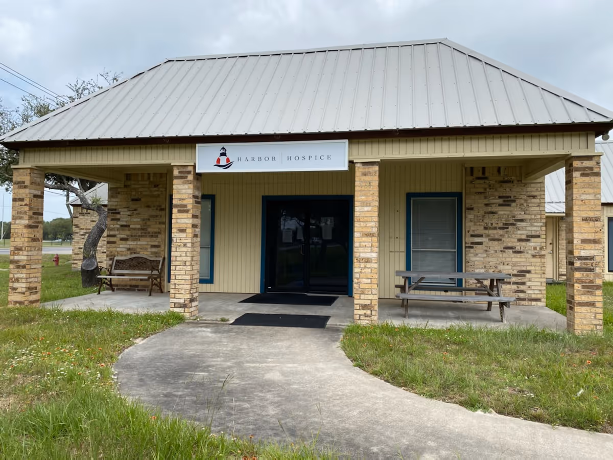 Small brick building with Harbor Hospice sign and outdoor seating on a porch.