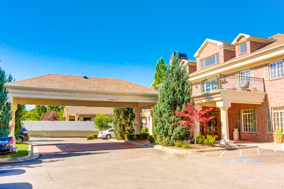 Brick senior living facility exterior with covered entrance, drive, and landscaped entryway.