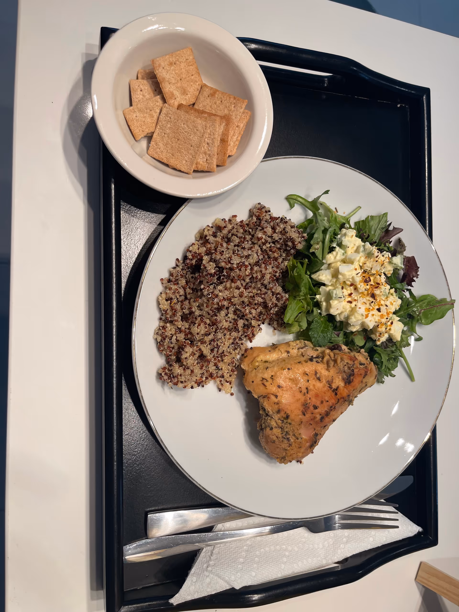 Meal on a tray featuring quinoa, greens salad, roasted chicken, and crackers.