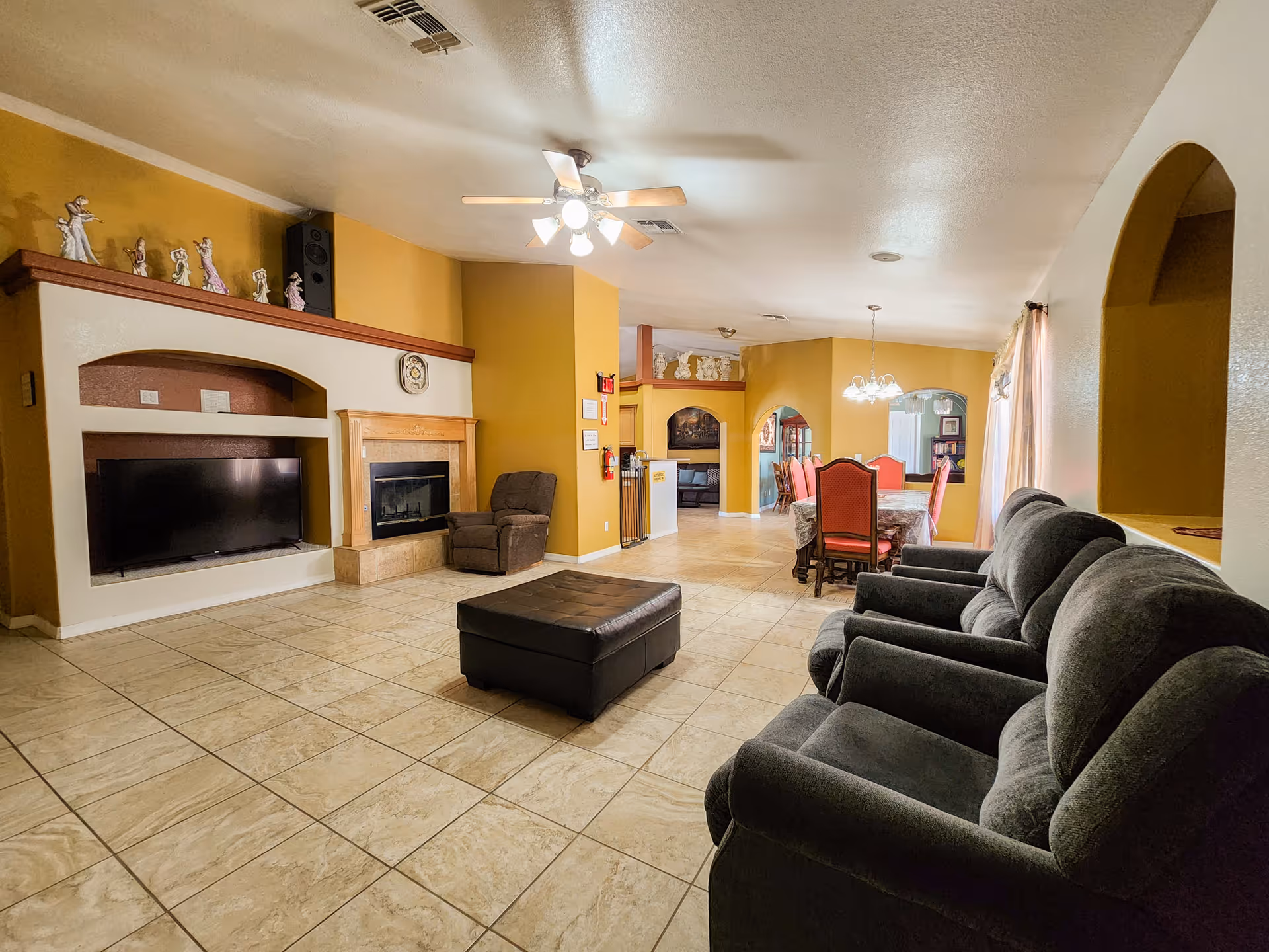 Spacious common living area with tiled floor, sofas, fireplace, and a dining area in the background.