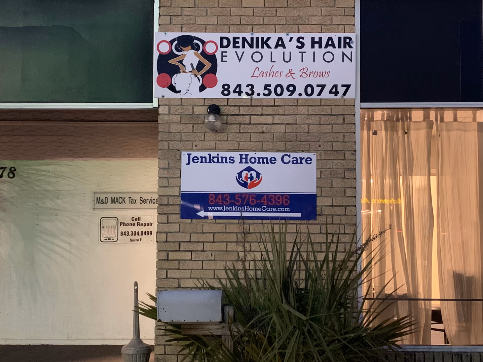 Brick building exterior with Jenkins Home Care sign and hair salon sign, window and plants.