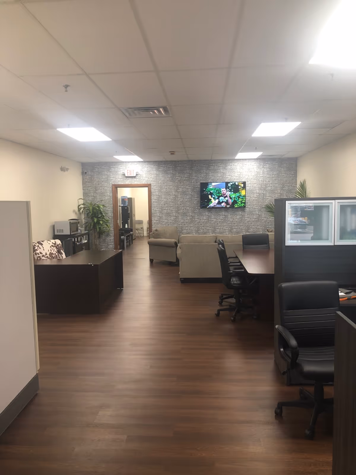 Interior lounge in senior facility with dark wood desks, couches, and a wall-mounted TV.