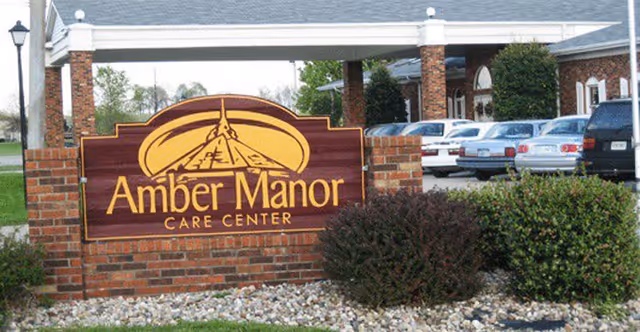 Amber Manor Care Center sign on brick near parking lot with shrubs and cars