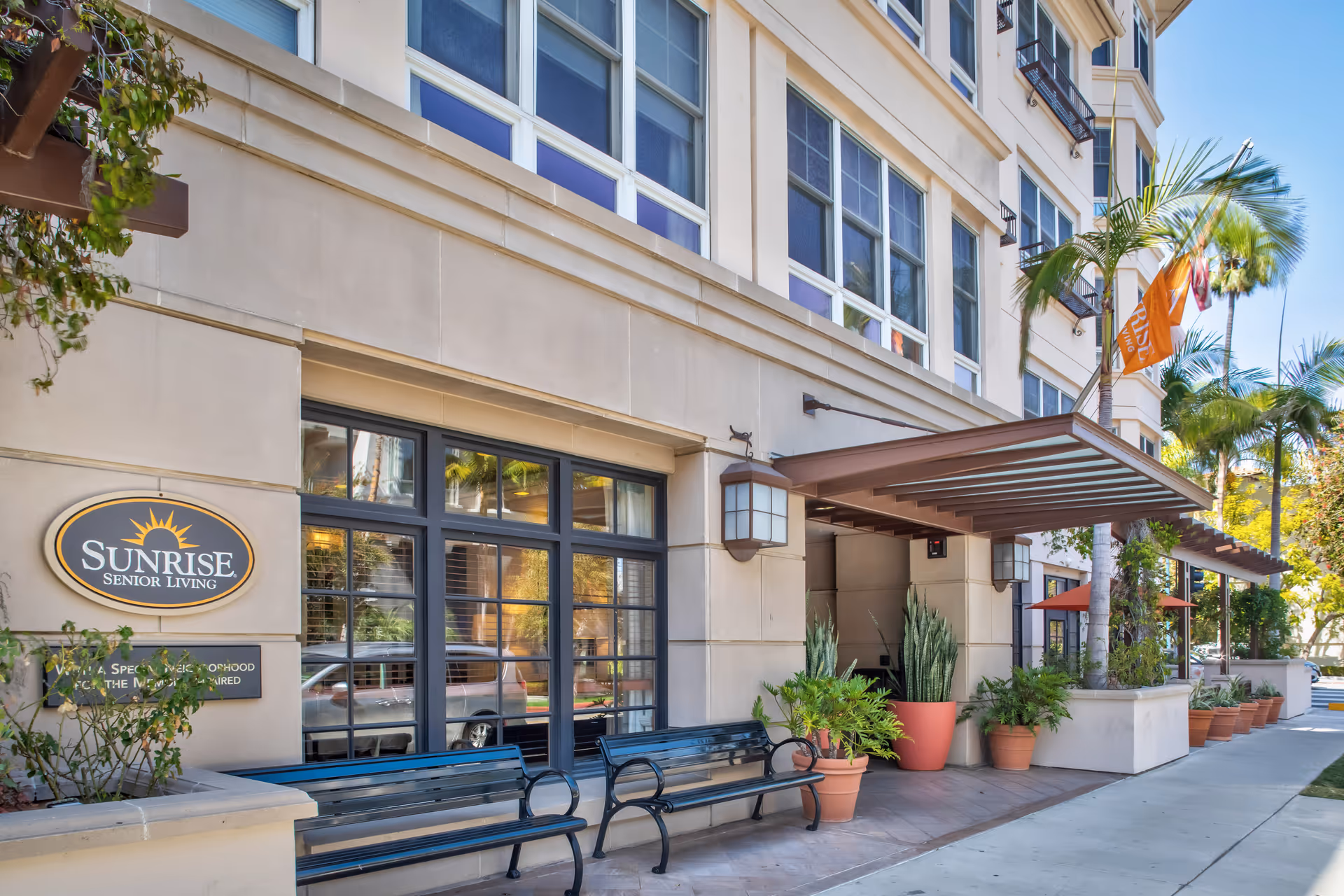 Sunrise of Beverly Hills entrance with glass doors, benches, and potted plants.