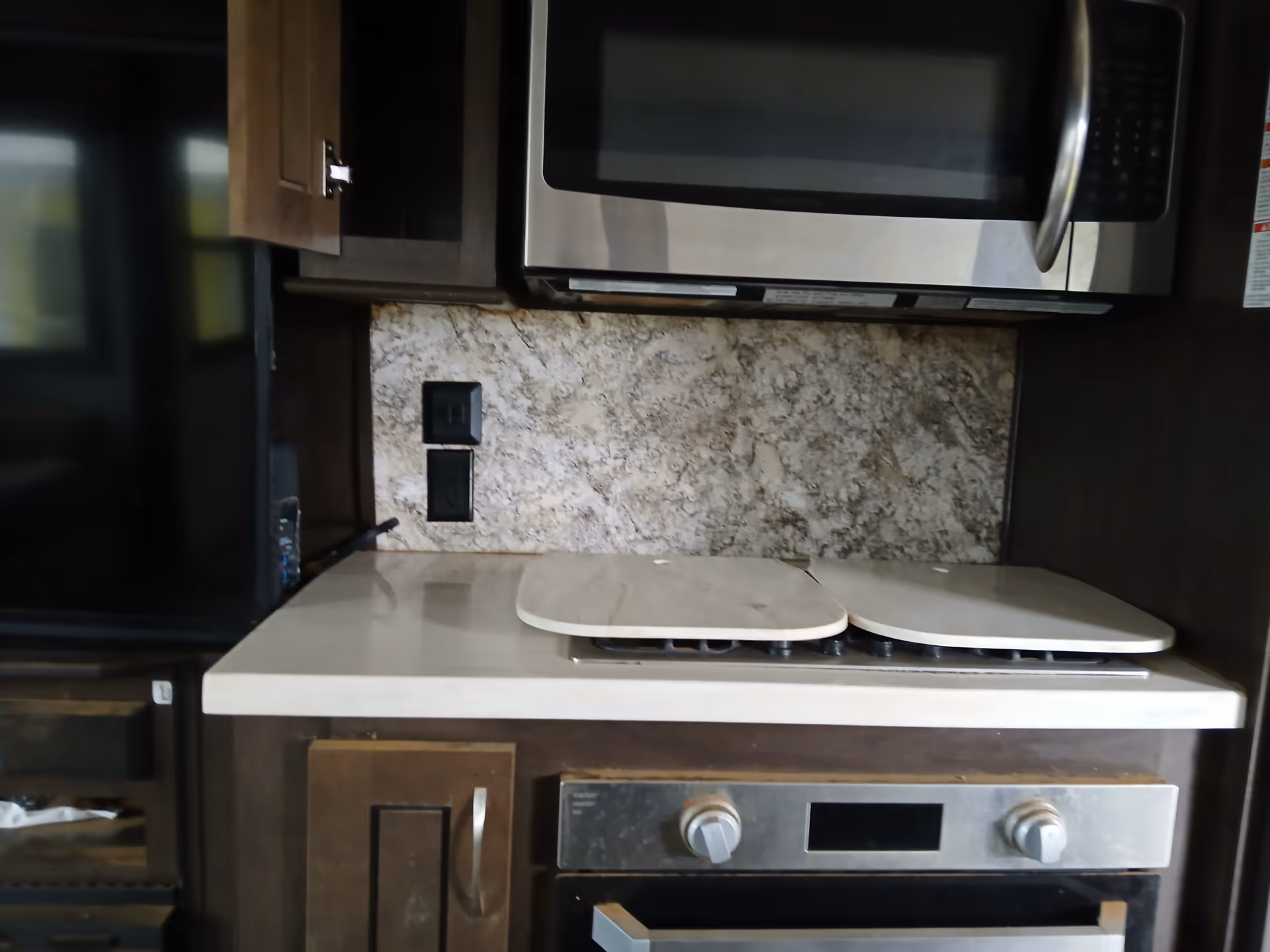 Compact kitchen with stainless microwave, stove, and granite backsplash.
