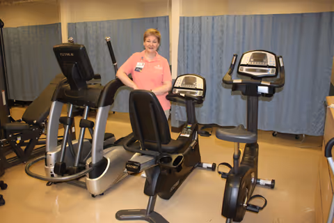 A staff member stands beside exercise equipment in a hospital gym.