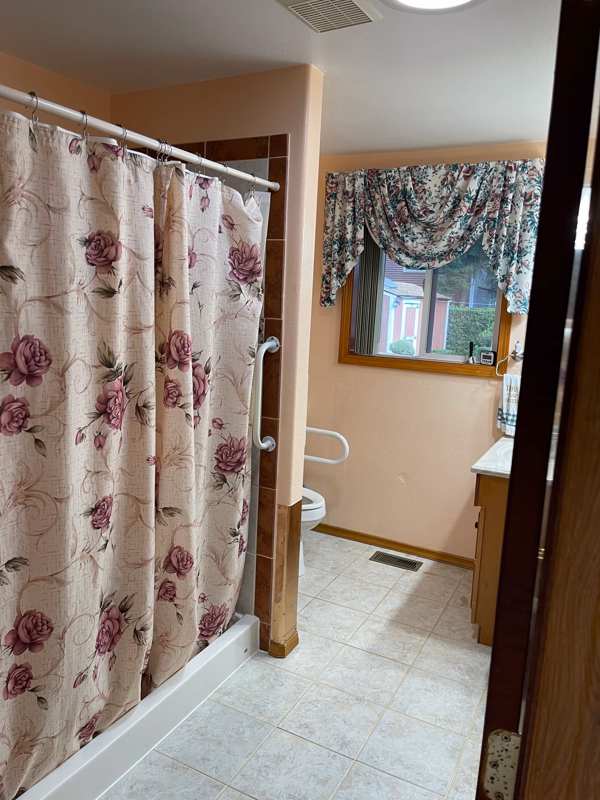 Bathroom scene with pink floral shower curtain, tub, toilet, sink, and window.