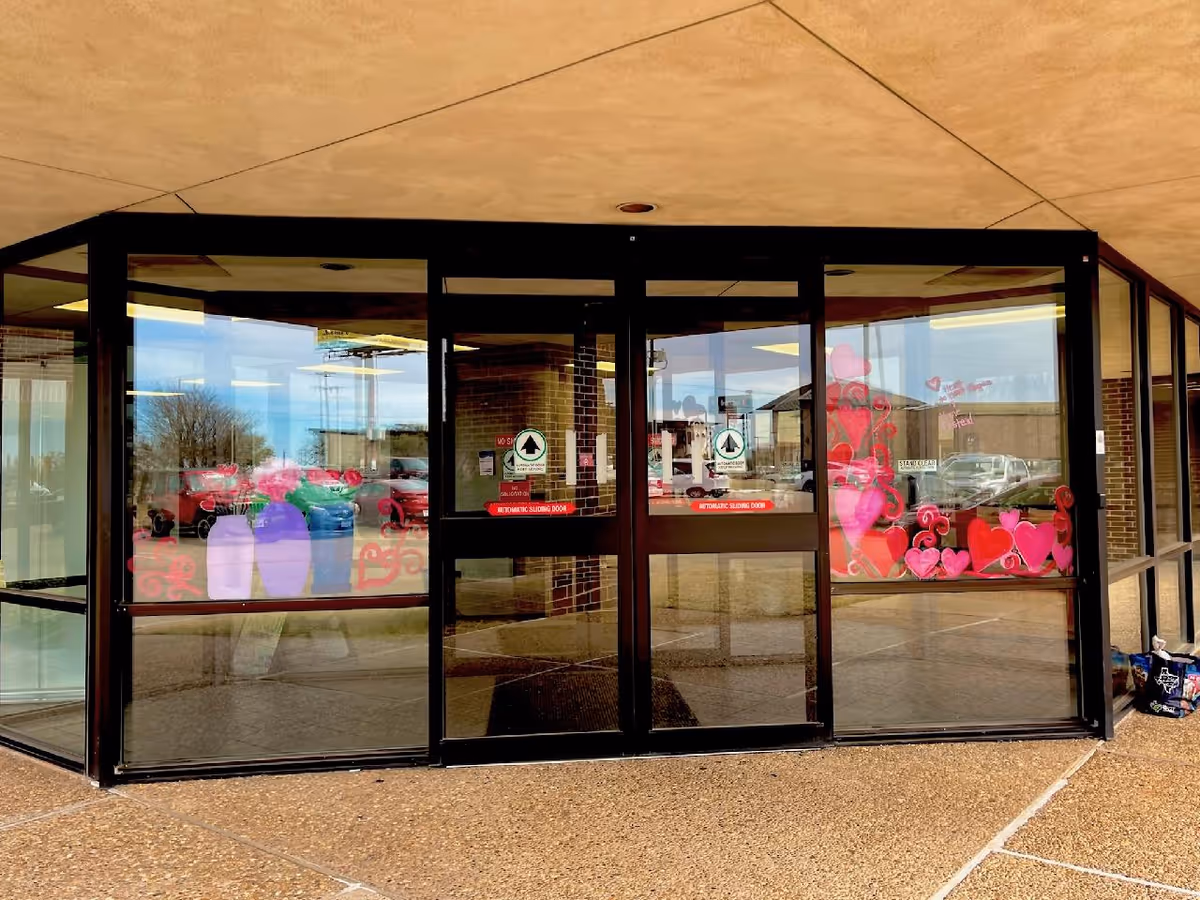 Glass entrance doors with pink heart decorations and brick exterior of the hospice facility
