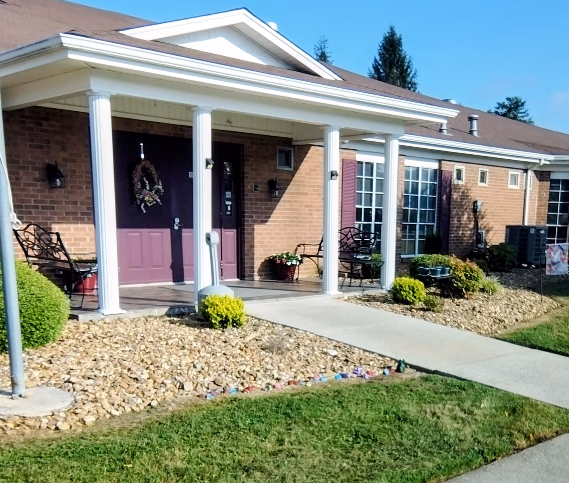 Brick senior living building with white columns, purple doors, and landscaped front yard.