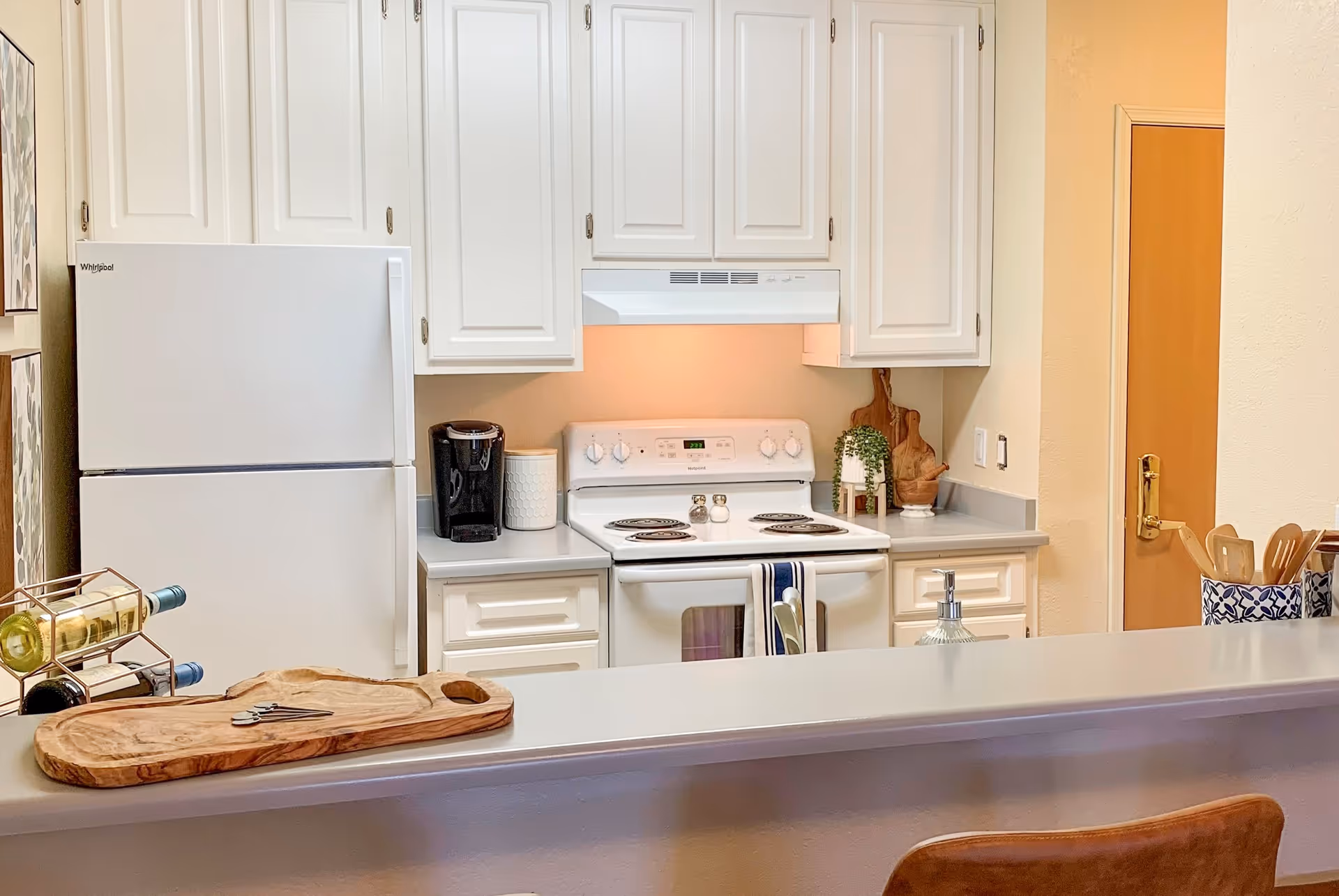 Bright kitchen with white cabinets, fridge, stove, and a counter with seating.