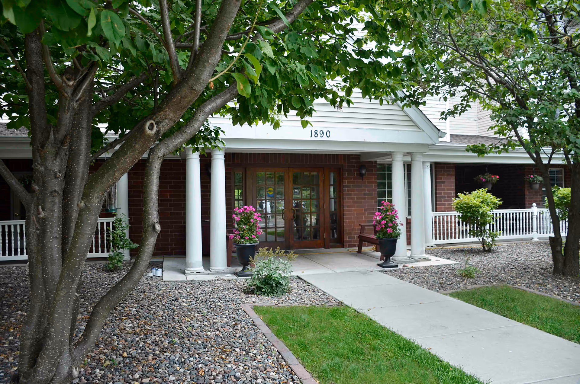 Front entrance of The Homestead at Maplewood with brick facade, columns, and potted plants.