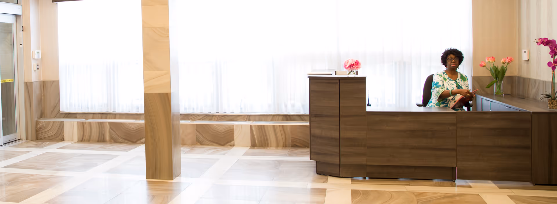 Reception area with a receptionist at a wooden counter in a bright lobby.