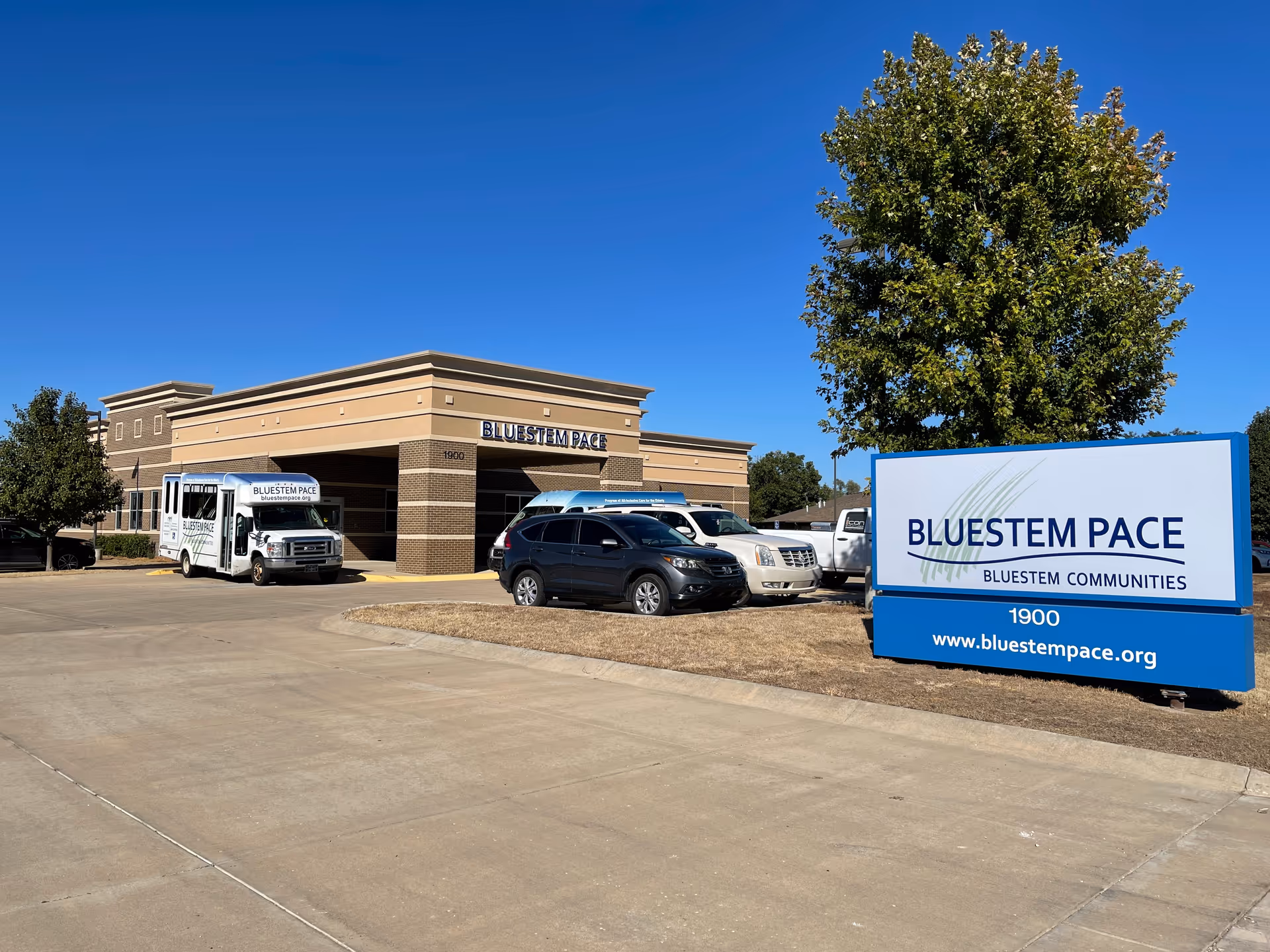 Bluestem PACE facility exterior with a sign and parked vehicles in lot.