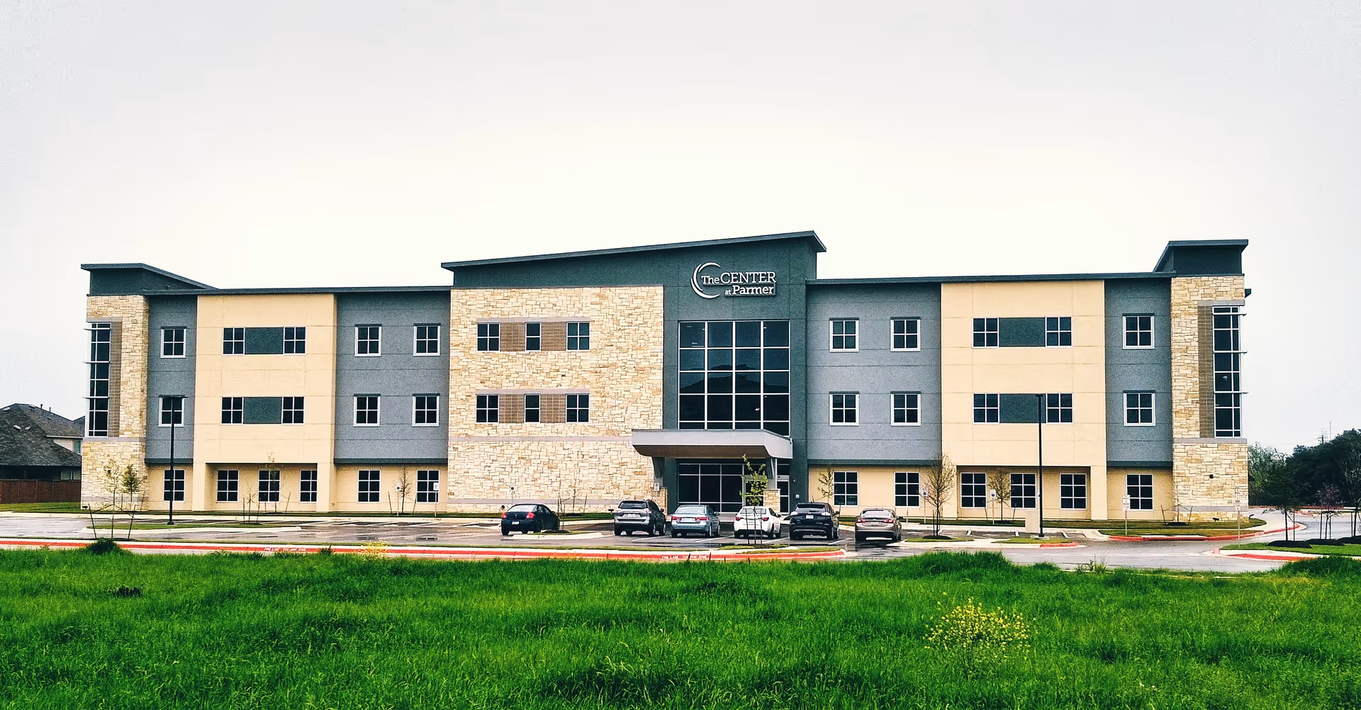 Exterior view of The Center at Parmer senior living facility with parked cars.