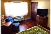 Cozy bedroom with window, air conditioner, chair, dresser, TV, and green bedspread.