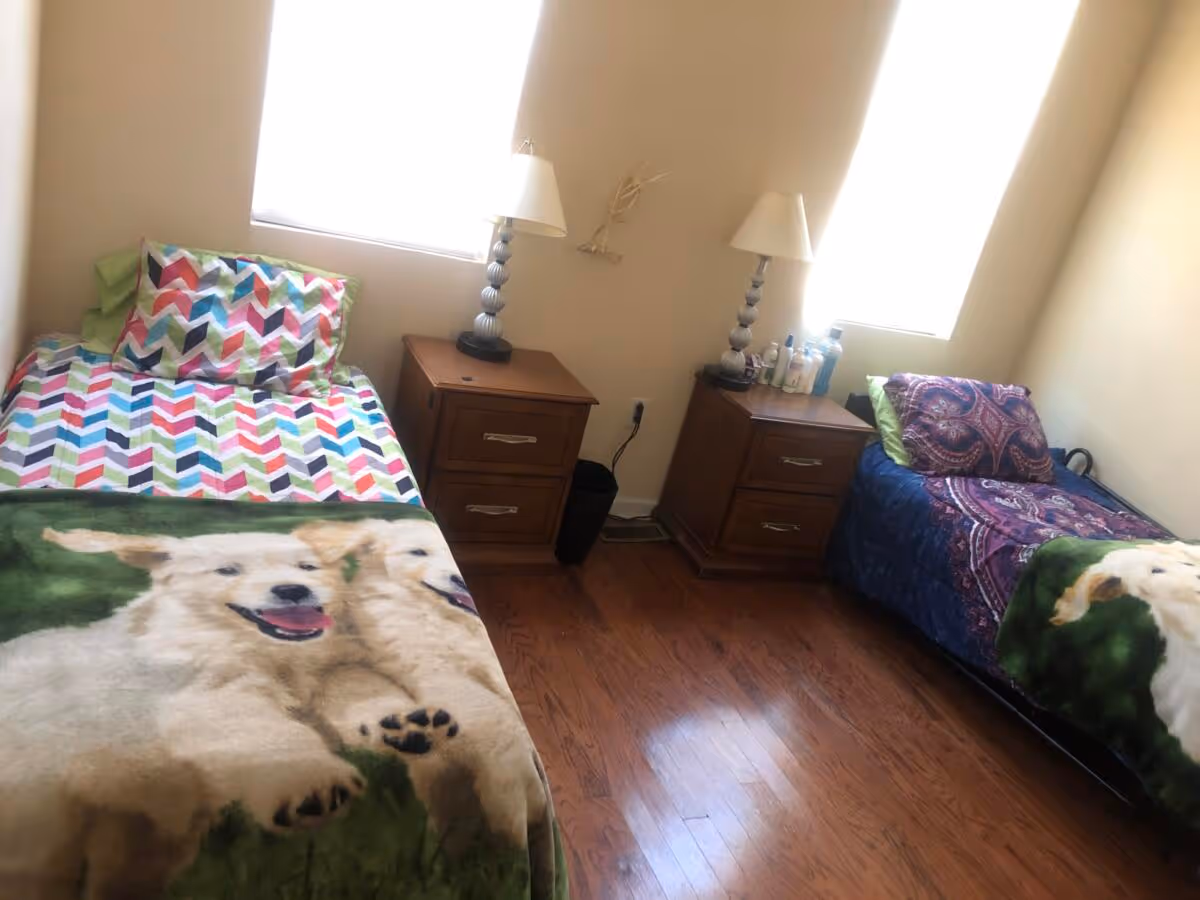 Two single beds with colorful blankets, nightstands, and lamps in a shared bedroom.